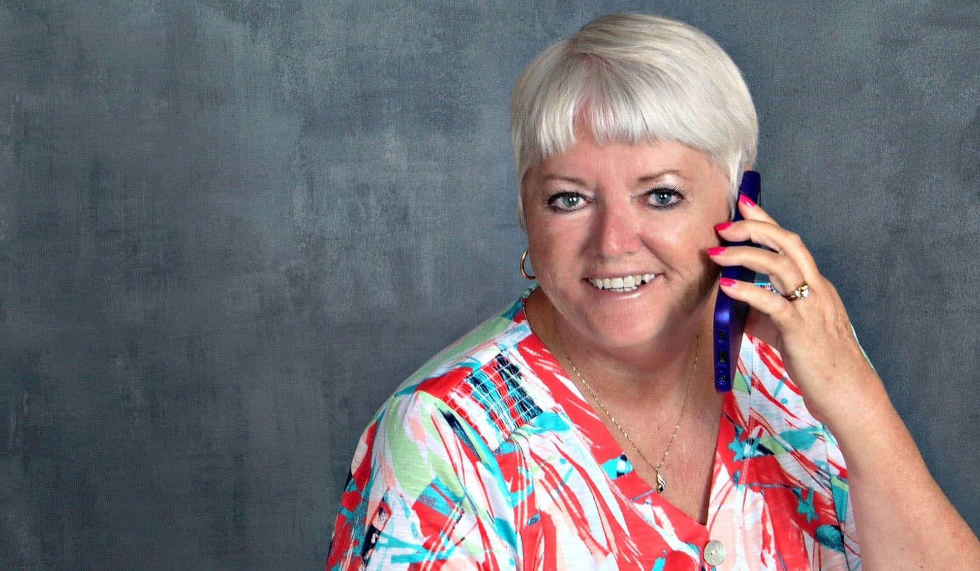 Gail Kenney smiling woman with short hair talking on the phone against grey background