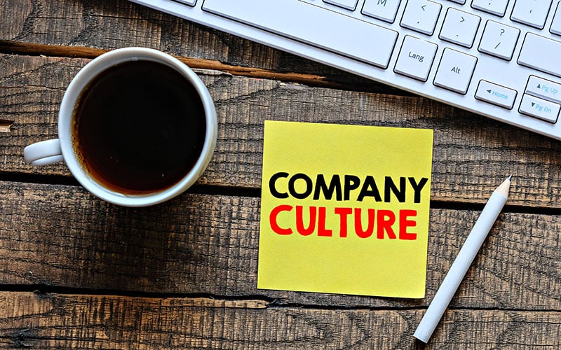 Cup and keyboard with 'Company Culture' sticky note on wooden desk