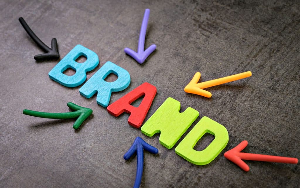 Colourful wooden letters spelling 'BRAND' with arrows on grey background