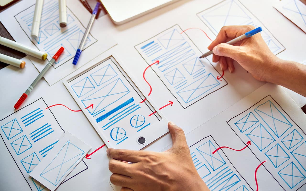 Person designing mobile app UI with sketches and markers