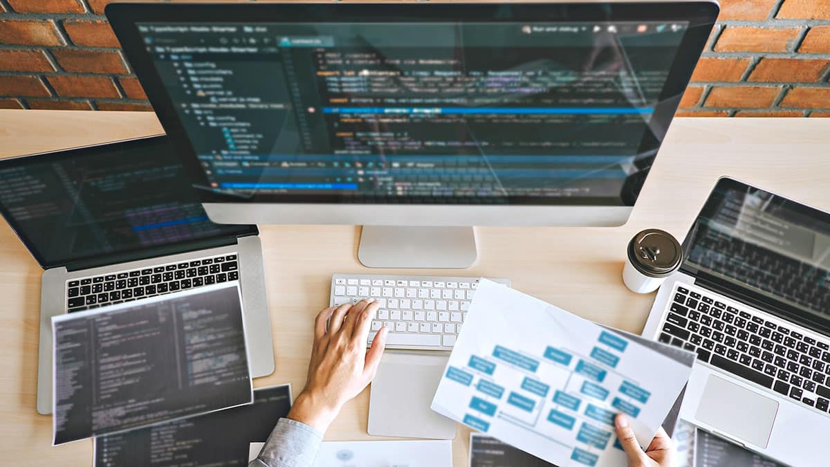 Developer reviewing code and workflow charts on multiple computers