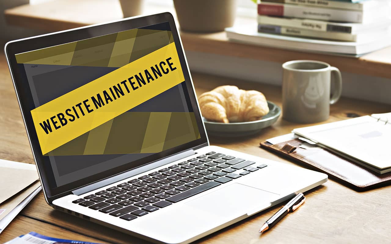 Laptop displaying website maintenance message with croissants on table