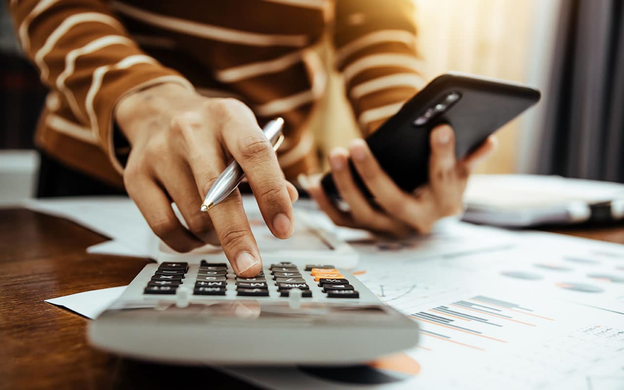 Person using calculator and smartphone on financial documents